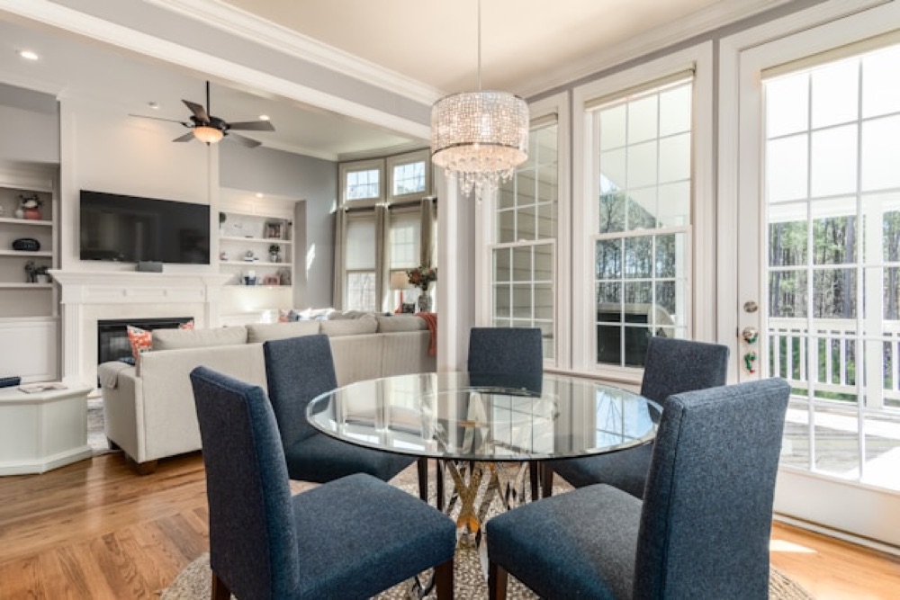 Sunlit breakfast room with built-in shelving, a chandelier, and blue upholstered chairs